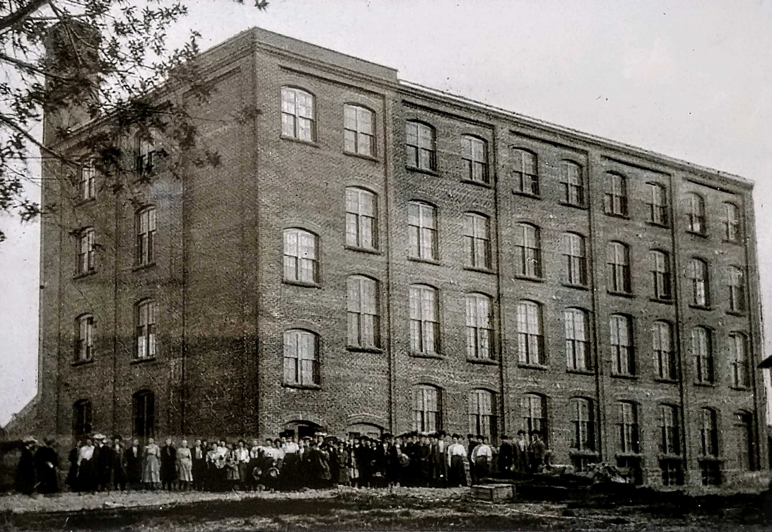 Black and white photograph of a factory building with a group of people in front.