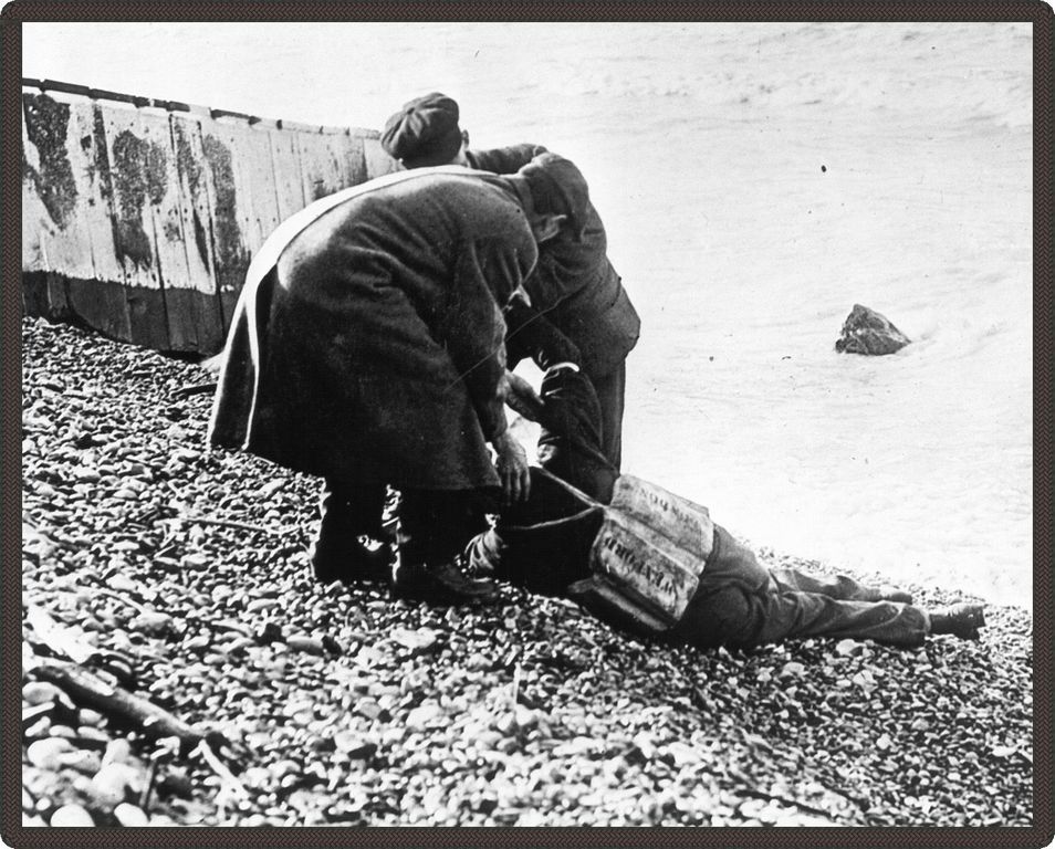 Black and white photo of two men moving bodies on the beach.