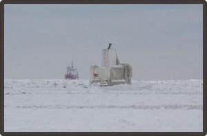 Photo of a building on the ice-covered lake with a lake freighter in the distance.