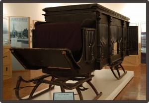 Horse-drawn wooden hearse on skis.