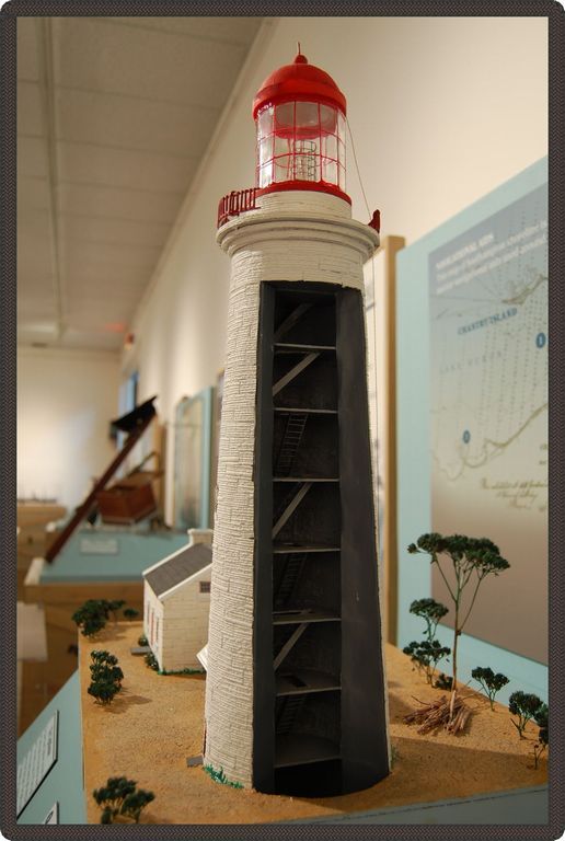 Close-up photo of a model of a lighthouse with a view inside lighthouse, with other items from the exhibit in the background.