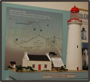 Model of a small house and large lighthouse in front of a map of different lighthouse locations.