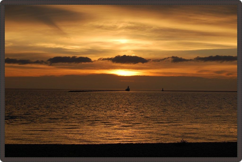 Photo taken from the beach showing a slightly cloudy orange sky above the lake.