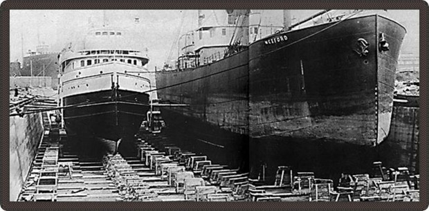 Black and white photo of two boats on dry land. Wexford is written on the side of the bigger boat.
