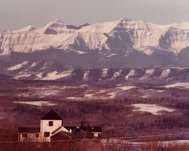 Colour aerial photo of black and white house with rolling hills and mountains in distance.