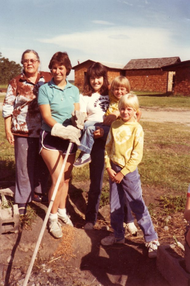 Colour photo of three adults and two children with outbuildings behind.