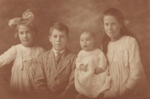 Sepia studio family photo of two young girls, boy and baby.