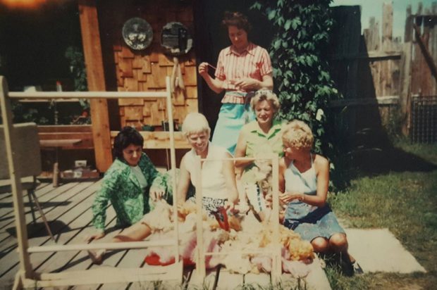 Colour photo of five women on deck with piles of raw wool and two looms.