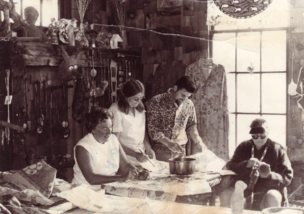 Black and white photo of three women and one man working in art studio filled with textiles and ceramics; bright window behind.