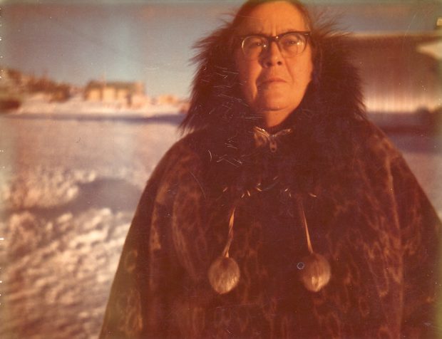 Colour photo of woman in glasses and fur coat with snowy town in background.