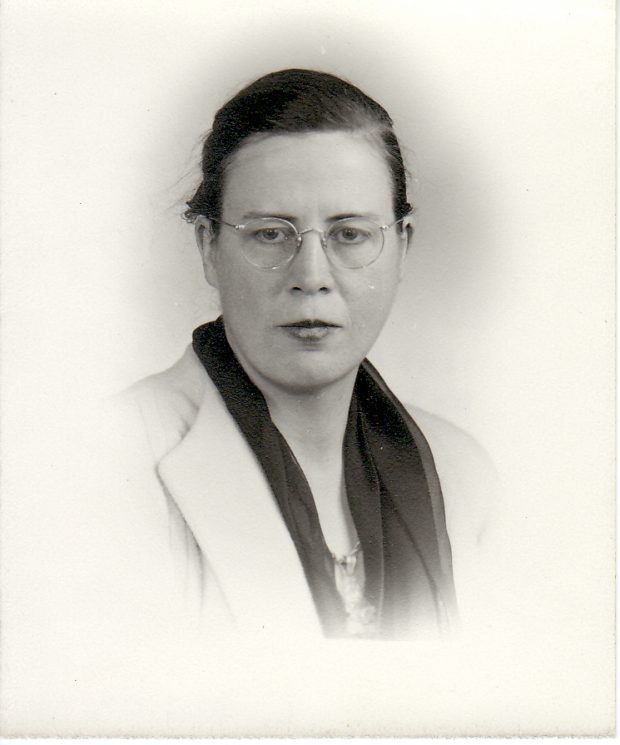 Black and white studio portrait of young woman with glasses, wearing dark scarf and light blazer.