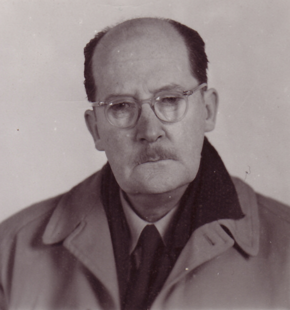 Black and white photo of an older man with glasses and a moustache wearing a coat and tie.