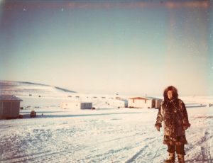 Colour photo of woman in fur coat with snowy town in background.