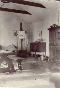 Black and white photograph of of a living room with high peaked ceiling and antique furniture and an easel