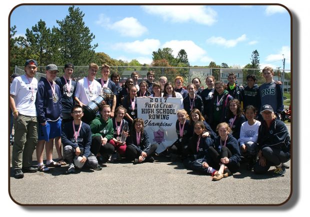 An image of a group of students from Rothesay Netherwood School who were awarded The Paris Crew trophy in the Summer of 2017. The students are holding up a banner which reads 2017 Paris Crew High School Rowing Champions. Each of the team members present in the photograph are wearing a medal around their neck with a pink ribbon lanyard.