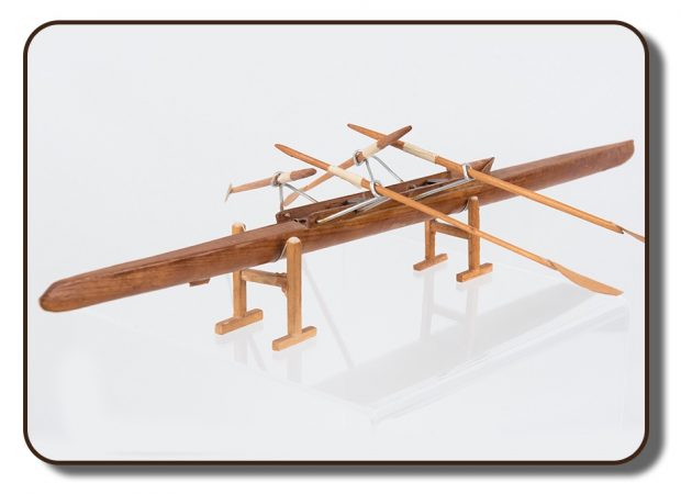 Image of a model of an early two-person rowing scull. This model is made of wood and measures approximately 10 inches long, there are four wooden oars attached by metal outriggers.