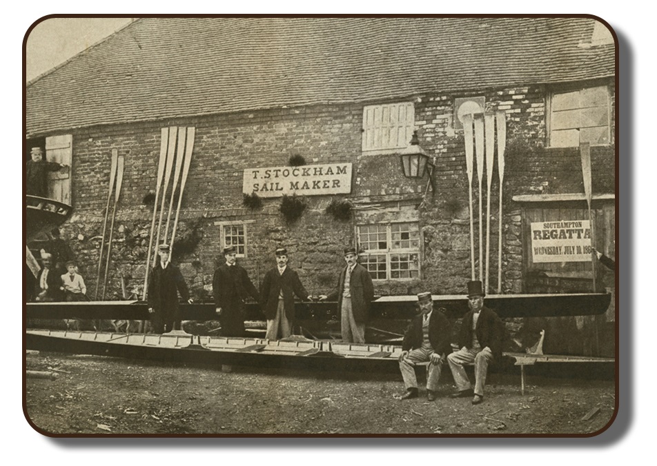 Image of the Paris Crew team members with their manager J. A. Harding posing in front of a boat house upon their arrival in Southampton, England. This black and white photo from July 1867 depicts a building made of stone blocks with their rowing scull positioned in front of the building, with rowing oars propped against its facade.