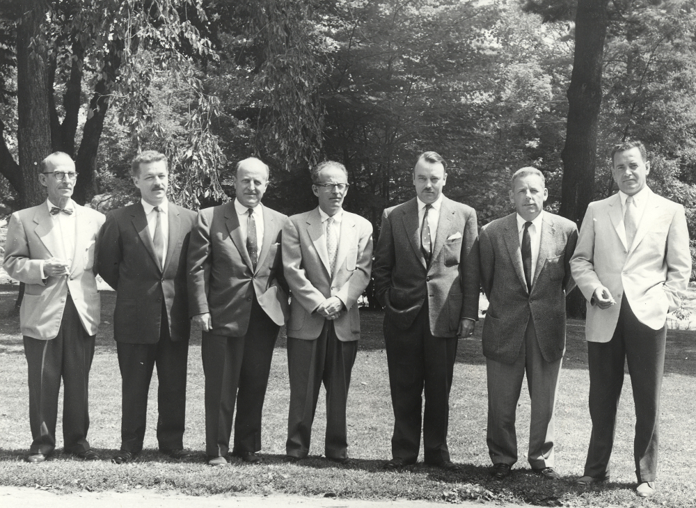 Black & white photograph of seven men standing together, outdoors.