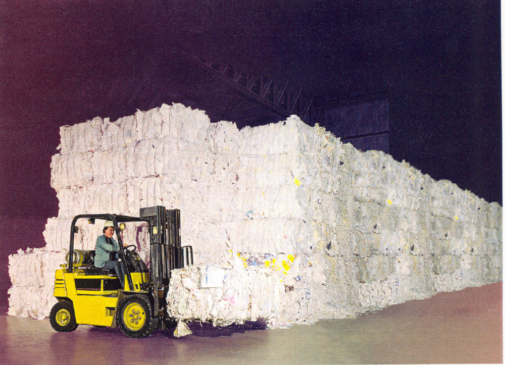 Colour photograph of a forklift in front of several piles of bales of scrap paper.