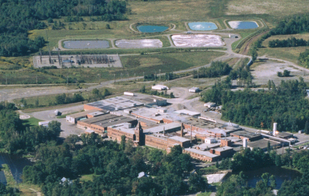 Photographie aérienne de plusieurs bâtiments de l’usine et du terrain environnant, dont les étangs aérés.