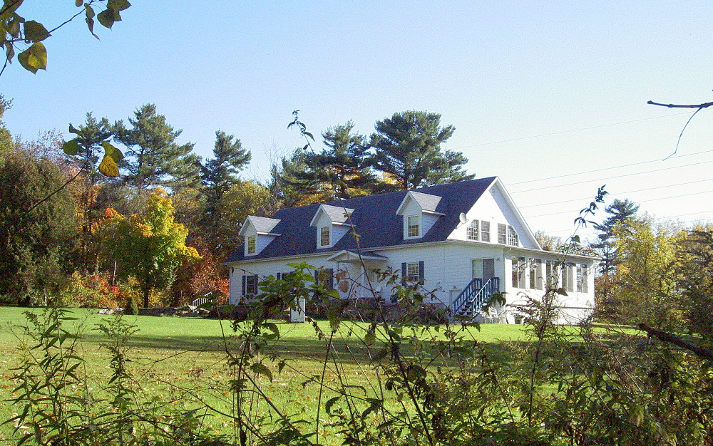 Photographie couleur d’une maison blanche à deux étages et de son terrain. 