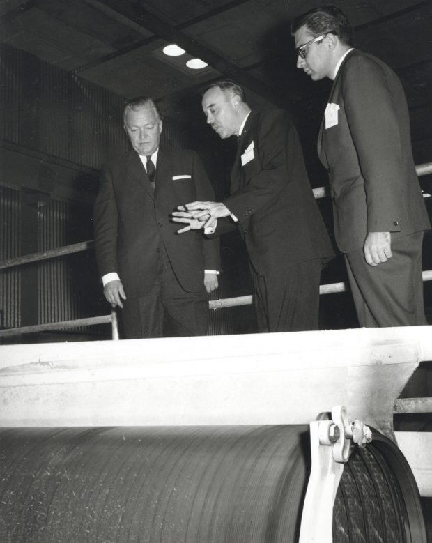 Black & white photograph of three men next to a large roll.