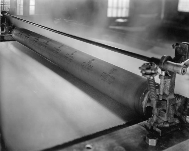Black & white photograph of a long roll with a sheet of paper passing below it.