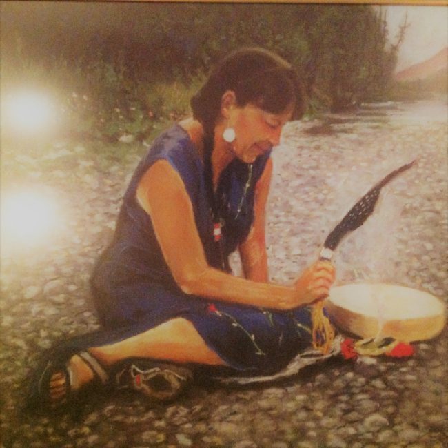 A painting of a woman wearing a blue dress with her dark hair in braids, her right hand holding a feather over a drum on the ground beside her.