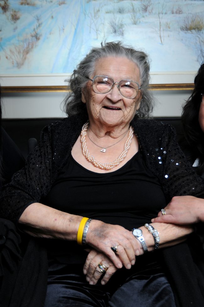 A woman in a wheelchair with four bracelets two on each wrist. She is smiling.