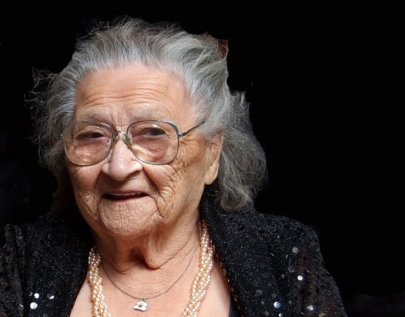 A coloured portrait of an elderly Jenny Flett wearing a black cardigan and glasses.