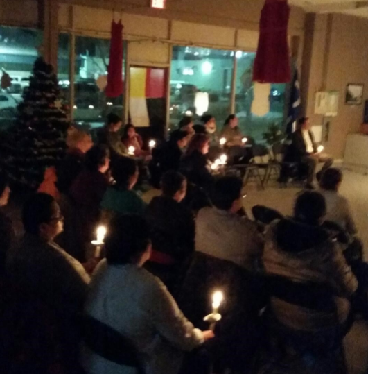 A group of people sitting down and holding candles facing toward the front.