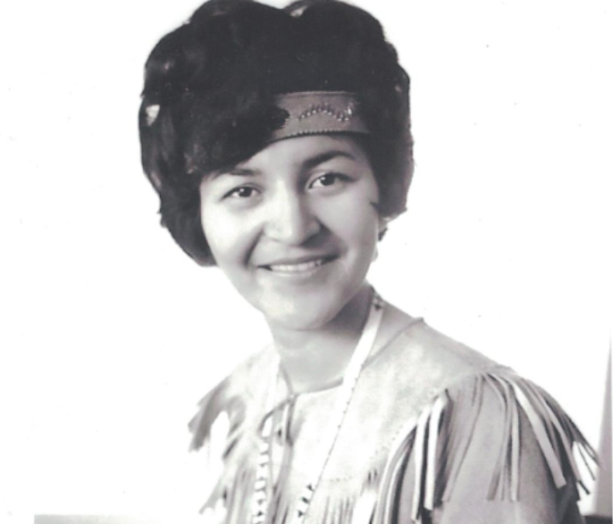 A black and white portrait of a young Dorothy McDonald with a headband around the top of her forehead with black short hair coming down, wearing a traditional dress looking straight ahead.