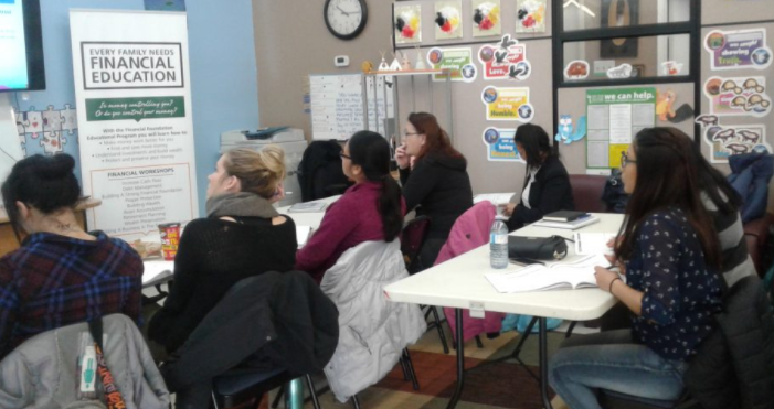 Coloured picture of group of women sitting in front of a white table looking straight ahead in front there is a banner that says Financial Education.