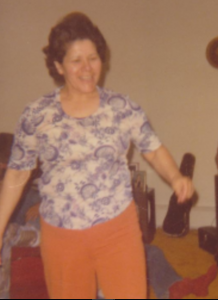 A middle-aged Berta shown dancing, wearing a paisley blue and white shirt with tan-coloured pants.