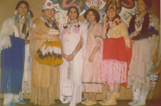 Six women dressed in traditional clothing smile at the camera.