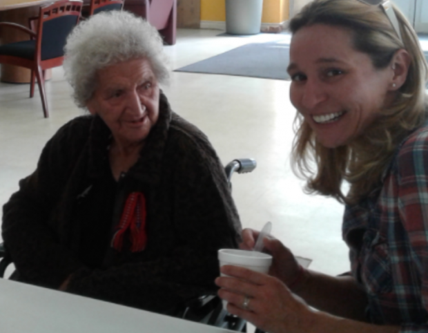 An elderly Violet Hansen sitting in a wheelchair looking at a younger woman smiling at the camera.