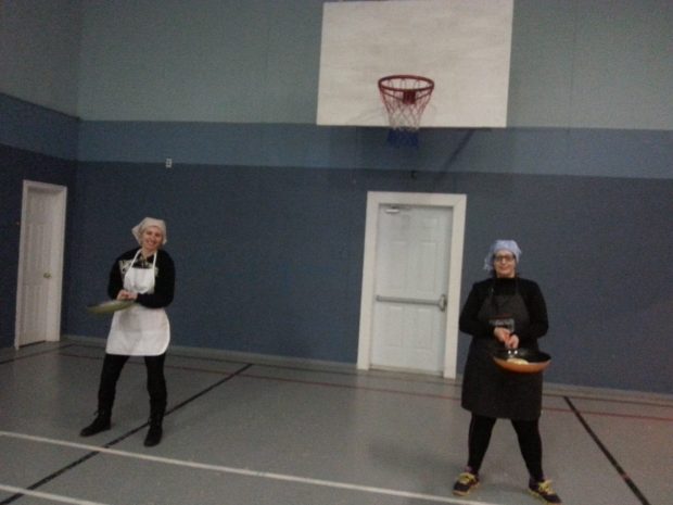 Two women stand with frying pans and pancakes ready for the pancake race