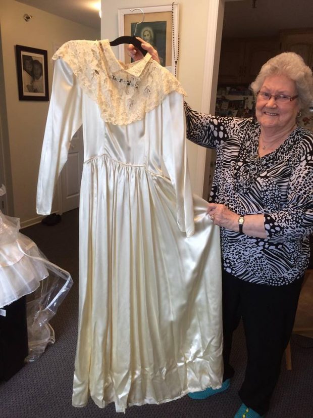 An elderly woman proudly shows her white satin wedding dress