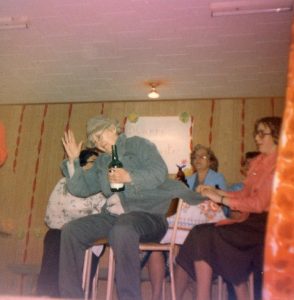 A woman holds a liquor bottle and with three other women perform a in a Christmas concert