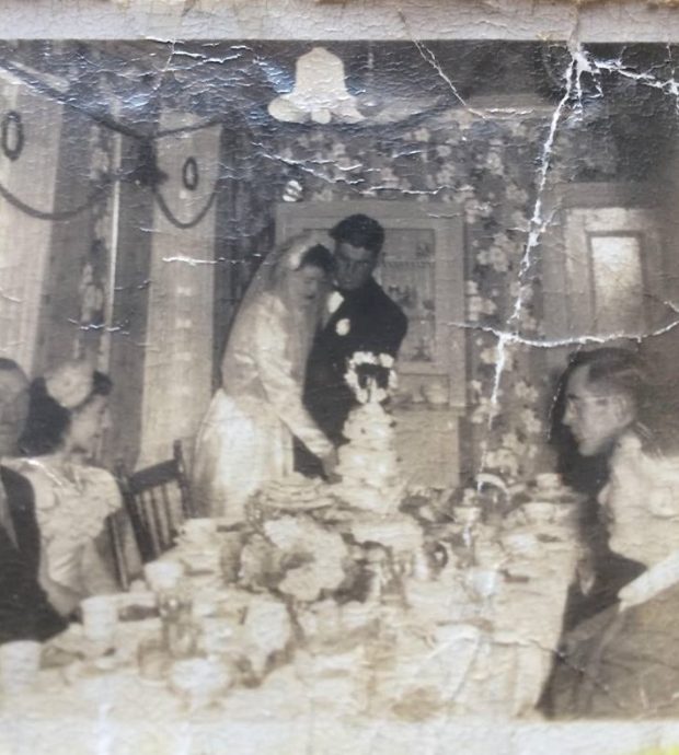 the bride and groom are shown cutting the wedding cake at Alice Drake's wedding supper in Oderin. guests and members of the bridal party look on.