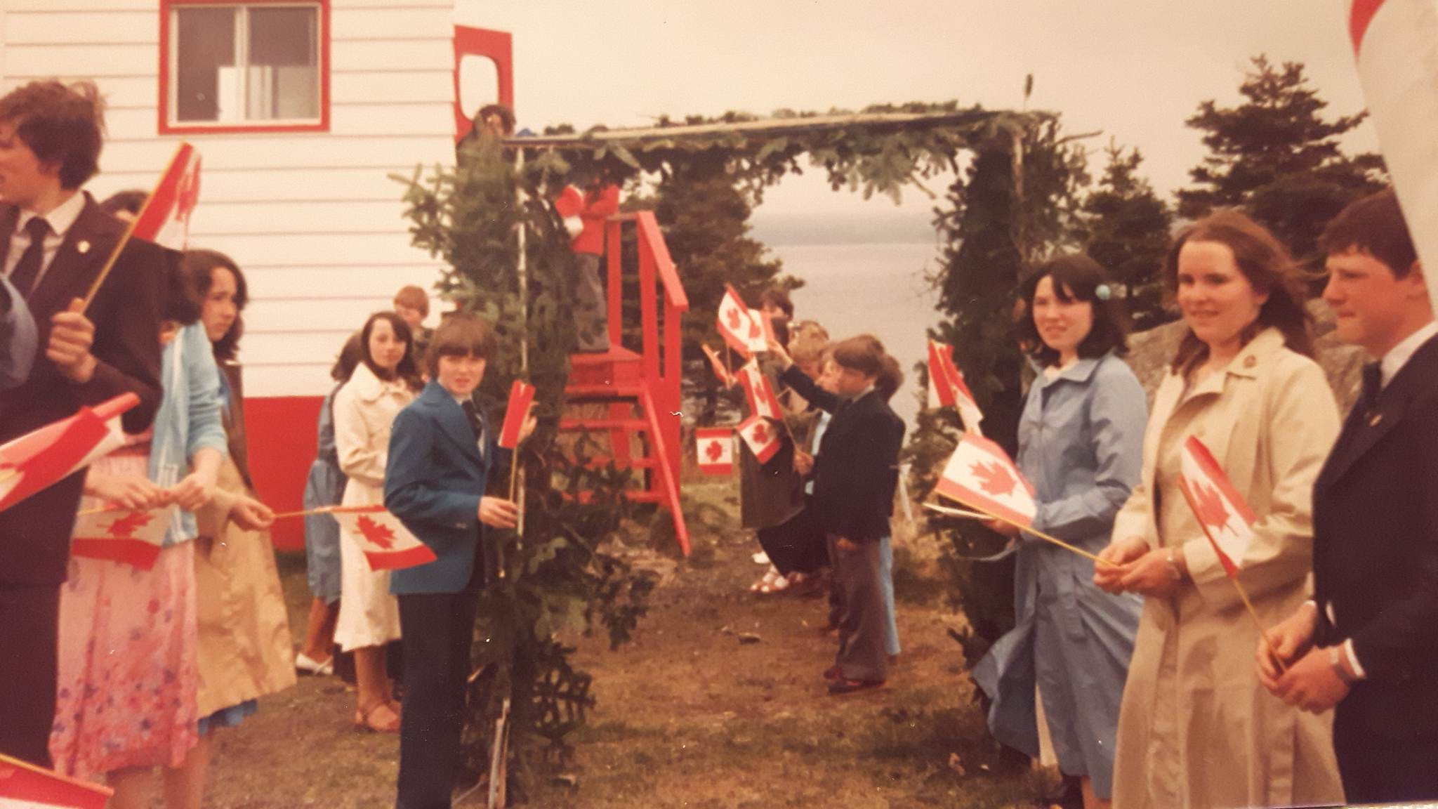 School children stand under an archway made of evergreen boughs awaiting the arrival of the bishop