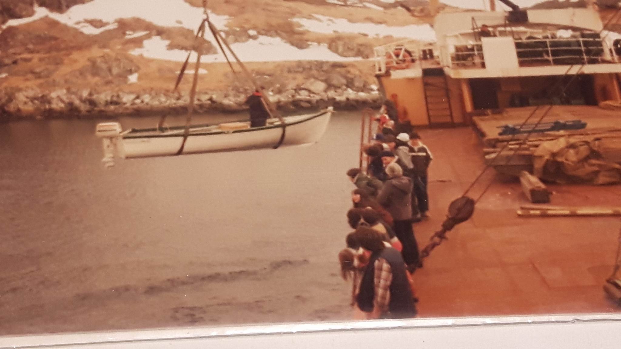 A small boat is lifted by a ferry as passengers wait on deck.