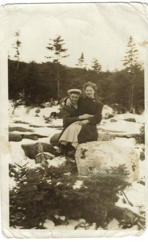 A man and a woman sit together on a rock in a brook