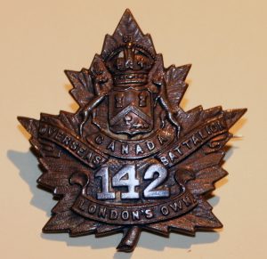 A badge in the shape of a maple leaf with a shield surmounted by a crown supported by two deer, scrolls and number 142.