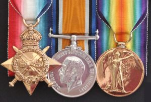 Three medals, mounted to bright coloured ribbons as follows (from left to right): first medal is golden shade, in the shape of a 4-pointed star, surmounted by a crown suspended to the ribbon by a ring, and with 2 swords intersected across; a laurel wreath is superimposed; second medal is silver shade, round shaped suspended to the ribbon on a bar; in the centre of the medal, a male profile looking to the left; the third medal is golden shade, round shaped, suspended to the ribbon by a ring; in the centre the image of a winged female, symbol of Victory.