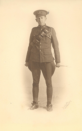 Photograph of a soldier standing and holding a whip behind with both his hands.