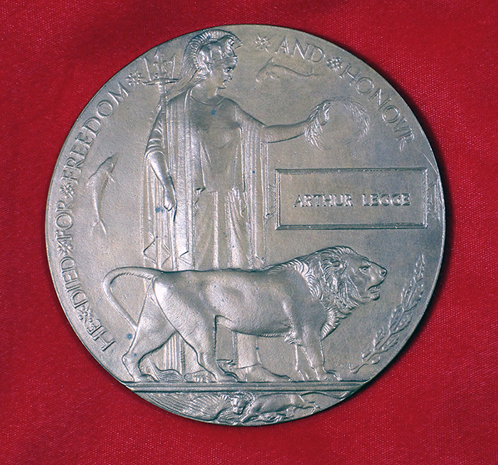 A circular brass plaque with the image of a women holding laurel leaves and a lion in front of her.