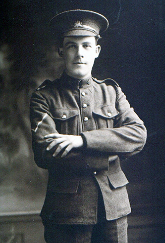 A soldier wearing a peak hat, with his arms in front oh his chest.