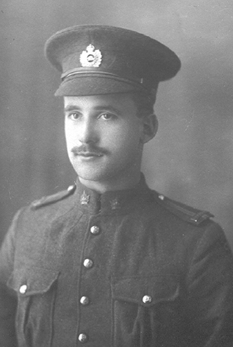 Portrait of a soldier wearing a peak hat. He has a moustache. Chest pockets, buttons and collar dogs can be seen.