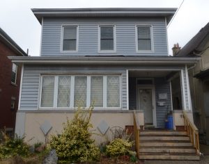 The front of a two story house with stairs on the left, a large window on 1st floor and 3 smaller windows on teh 2nd floor.